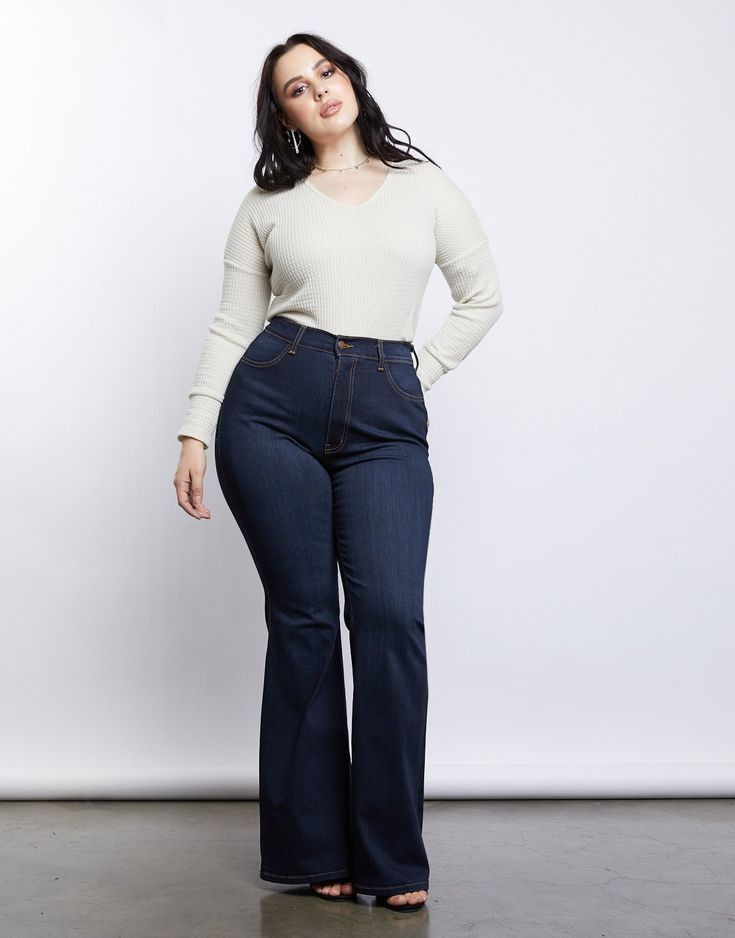 Woman with dark hair wearing a long sleeve shirt and flared jeans in a studio