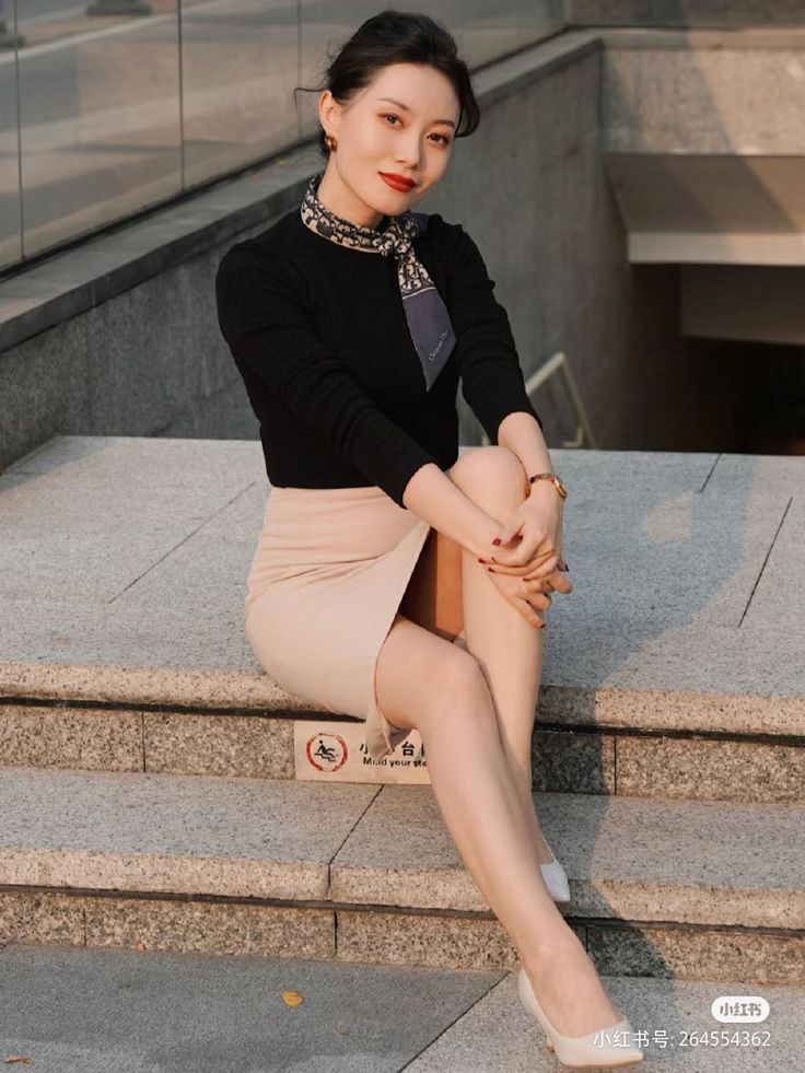 Woman in a black top and beige skirt sitting on outdoor stairs