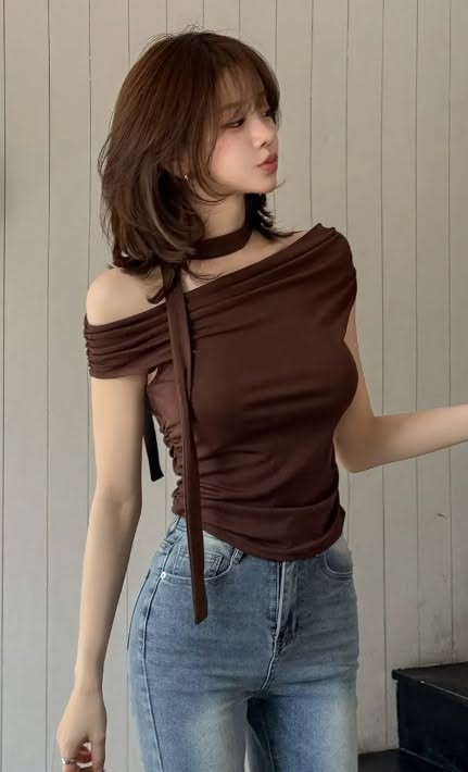 Woman with brown hair wearing an off-shoulder top and blue jeans indoors