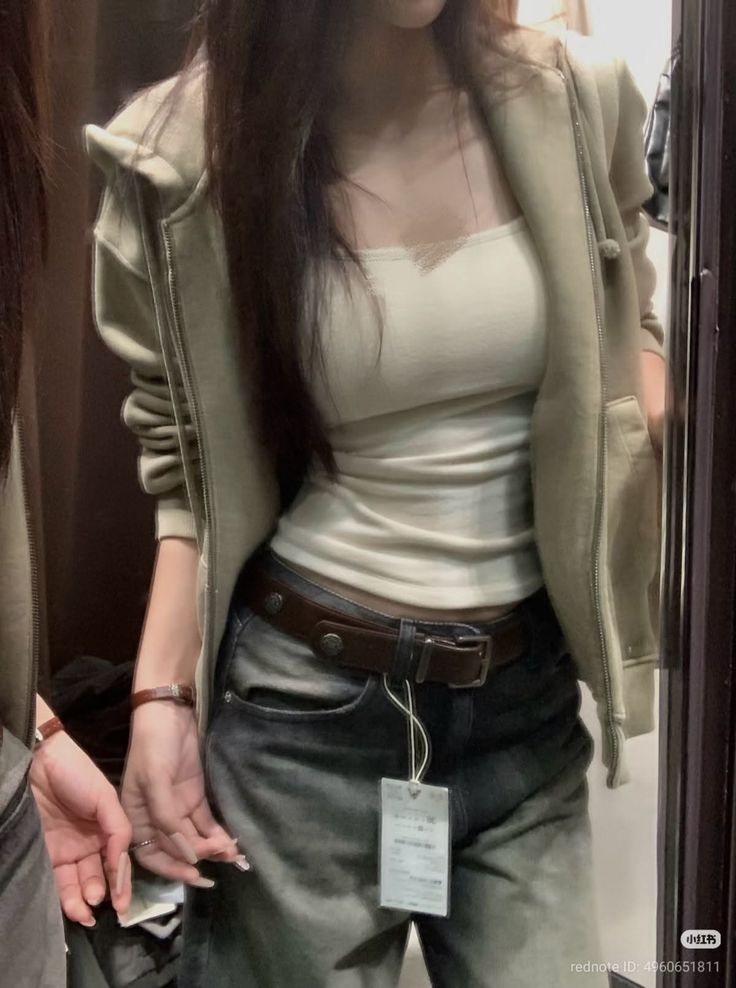 Woman in a hoodie and jeans with a crop top, reflected in a mirror