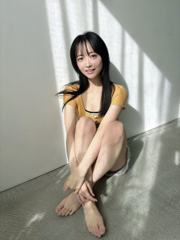 Woman with long black hair sitting on the floor in a yellow top and shorts