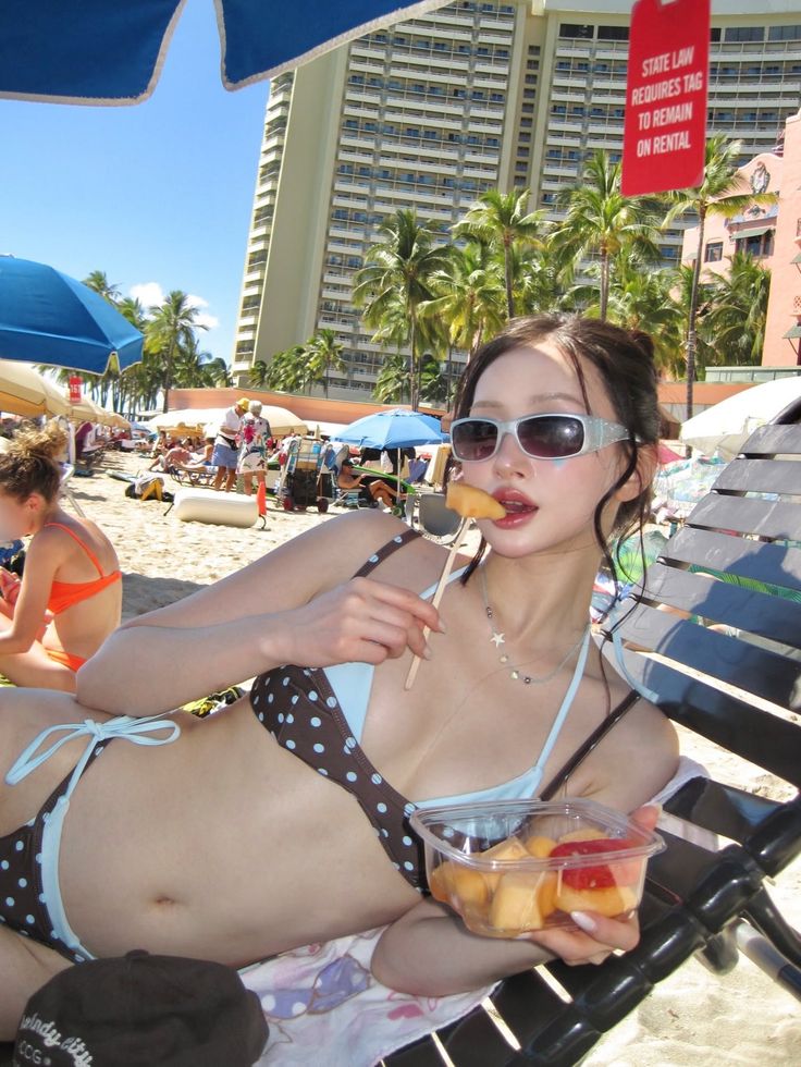 Woman in a polka dot bikini eating fruit on a beach chair
