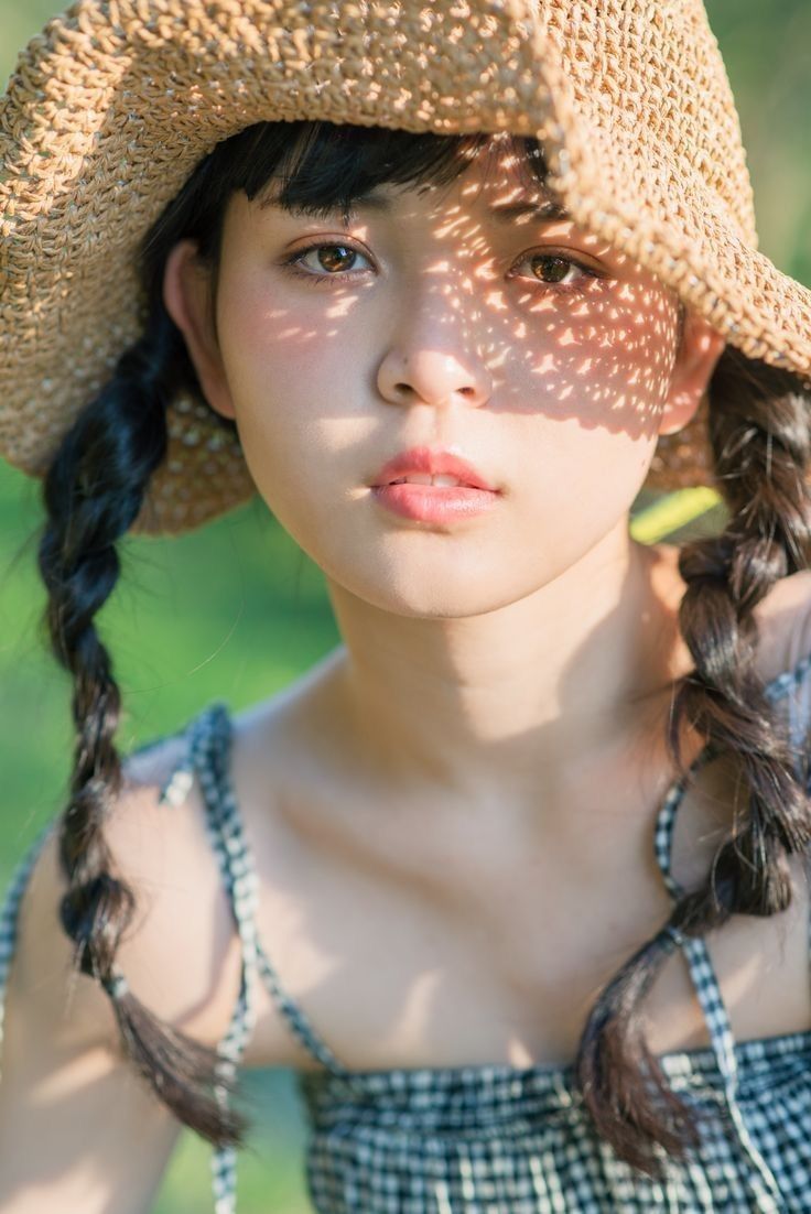 Woman in a straw hat and gingham dress with sunlight casting shadows on her face