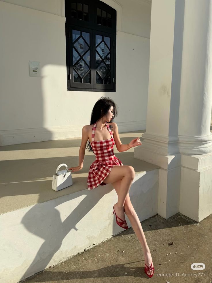 Woman in a red plaid dress and high heels sitting outdoors in soft lighting
