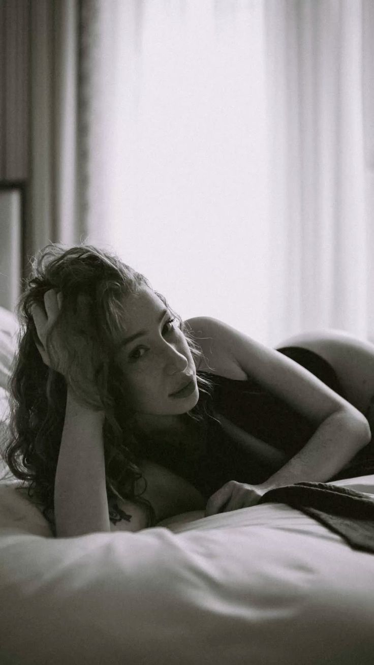 Woman with curly hair lying on a bed in black and white