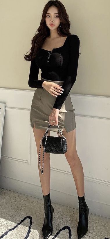 Woman in a black long-sleeve top and mini skirt holding a quilted bag