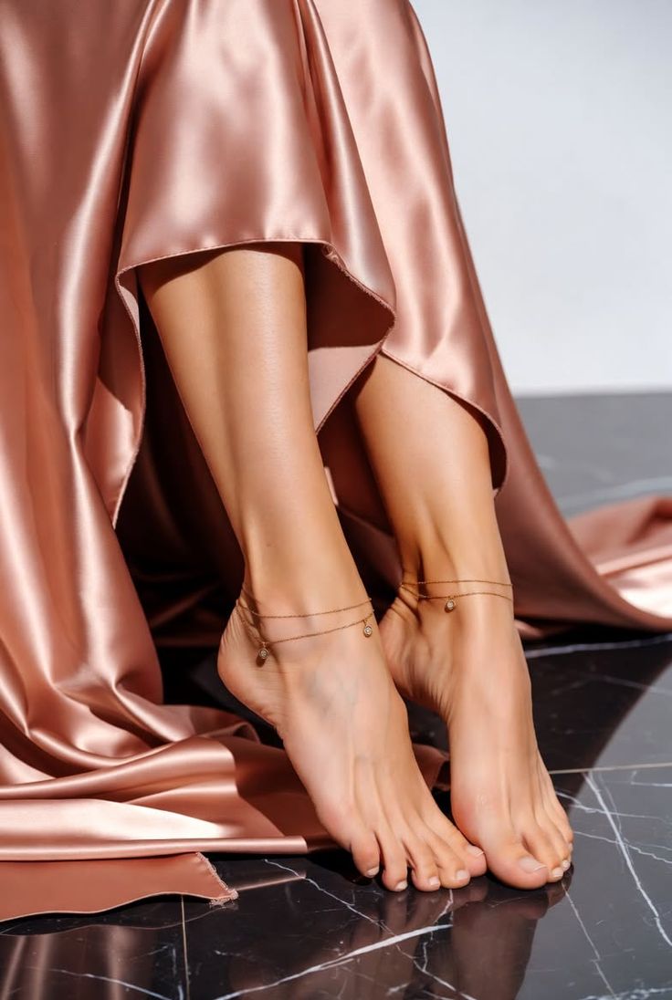 Bare feet with anklets on a dark marble floor, surrounded by satin fabric