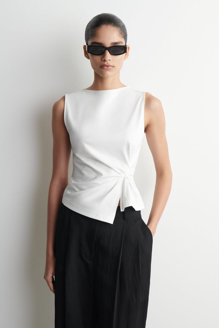 Woman in a white top and black pants wearing sunglasses in a studio