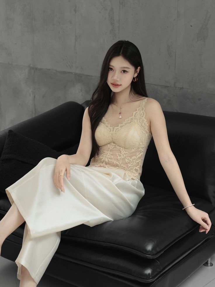 Woman with long black hair wearing a lace top and satin pants on a black couch
