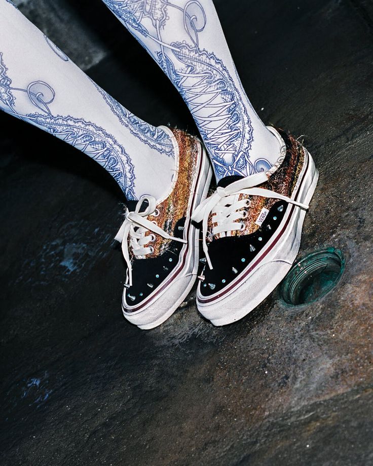 Person wearing patterned tights and sneakers on a dark floor