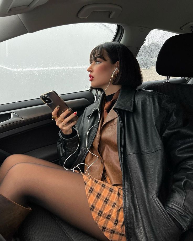 Woman with short hair in a car, wearing a leather jacket and plaid skirt