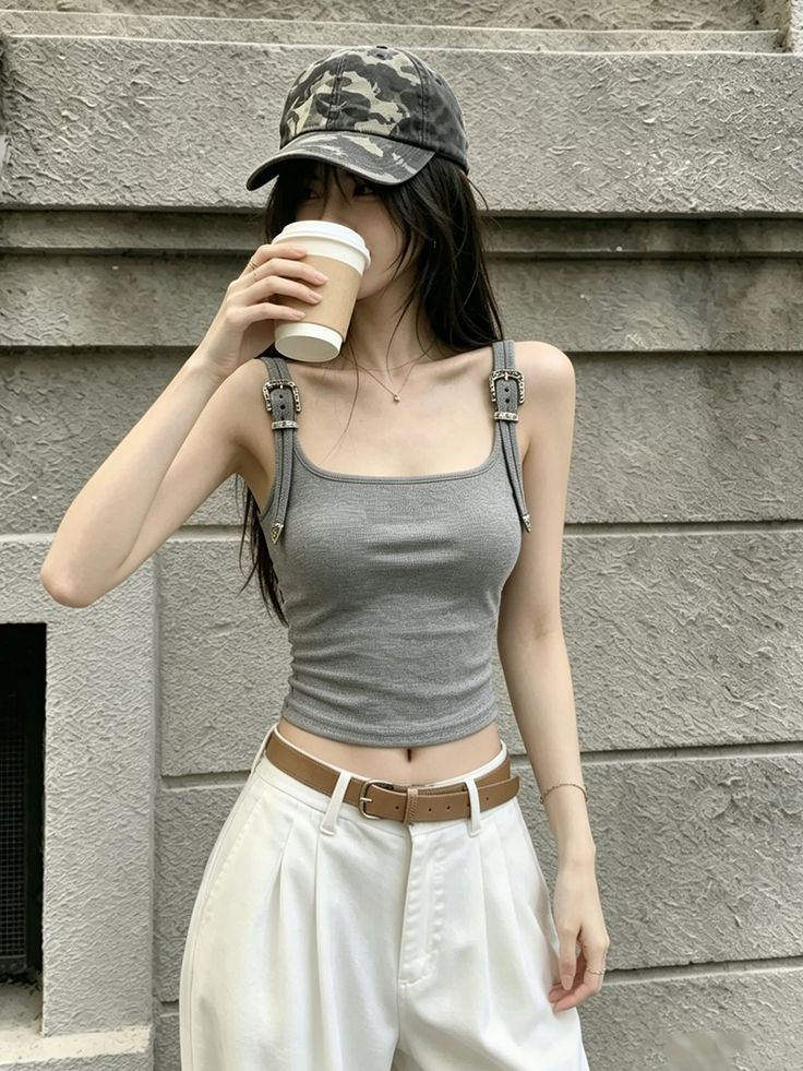 Woman in a camo hat and gray tank top drinking from a cup outdoors