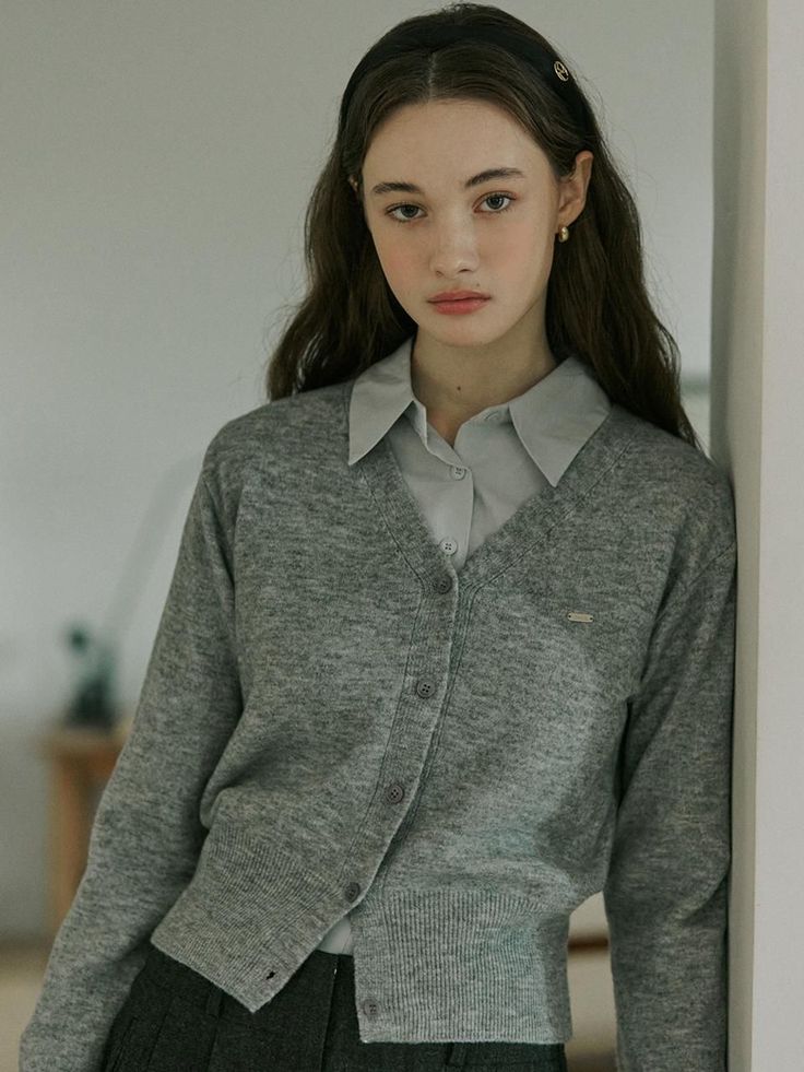 Woman with long hair wearing a gray cardigan and collared shirt indoors