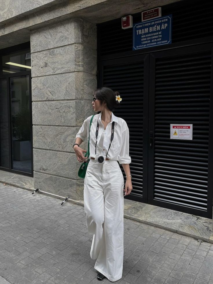 Woman in a white shirt and wide leg pants with a camera on a street