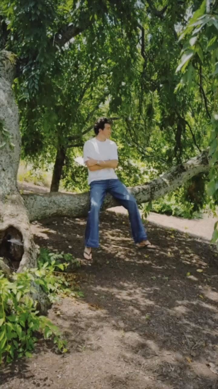 Man in a white t-shirt and blue jeans sitting on a tree branch outdoors