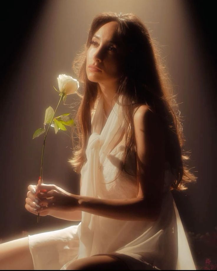 Woman with long hair holding a white rose in dramatic soft lighting