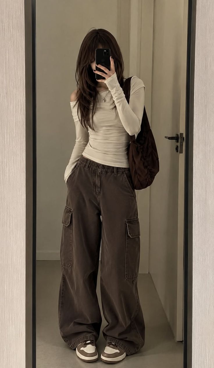 Person with long hair taking a mirror selfie in an off-shoulder top and cargo pants