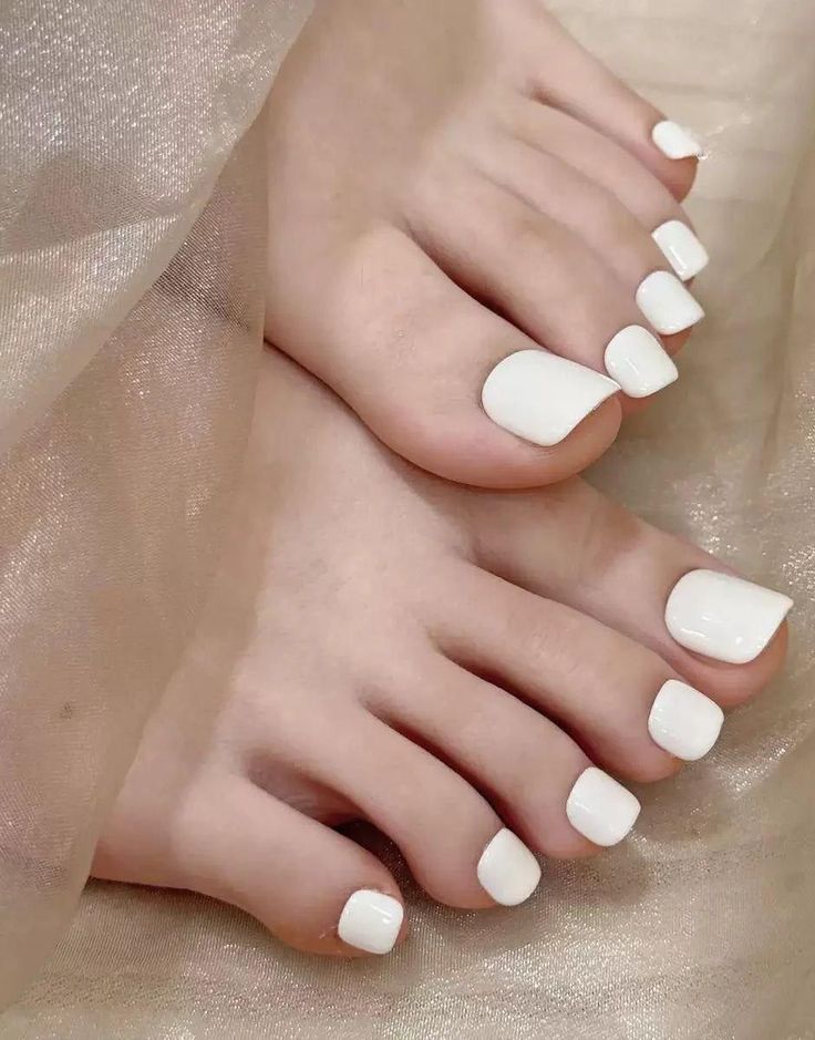 Close up of feet with white painted toenails on a soft fabric surface