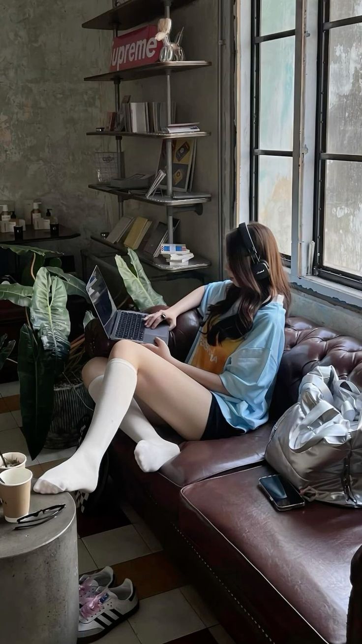 Woman with long hair and headphones using a laptop on a brown couch