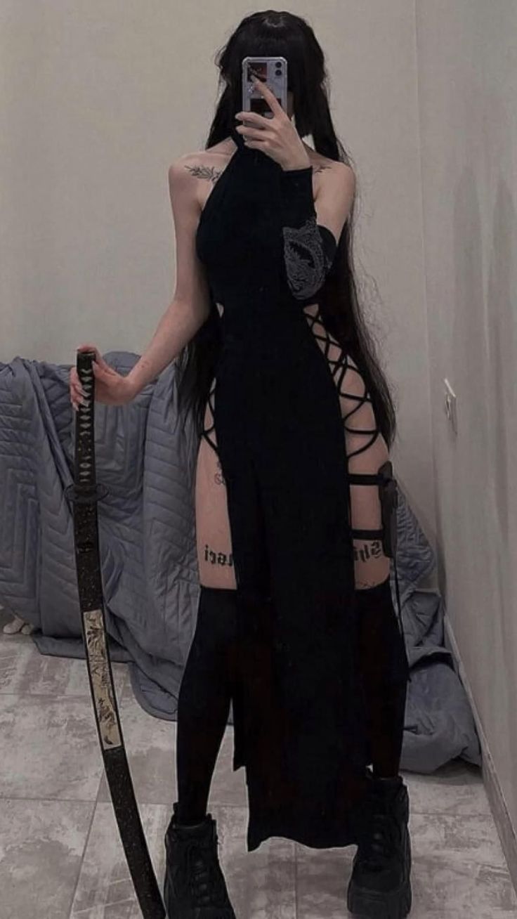 Person in a black dress with exposed skin and a katana, taking a mirror selfie