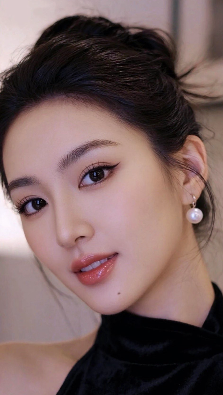 Woman with black hair in an updo wearing pearl earrings and glossy lips