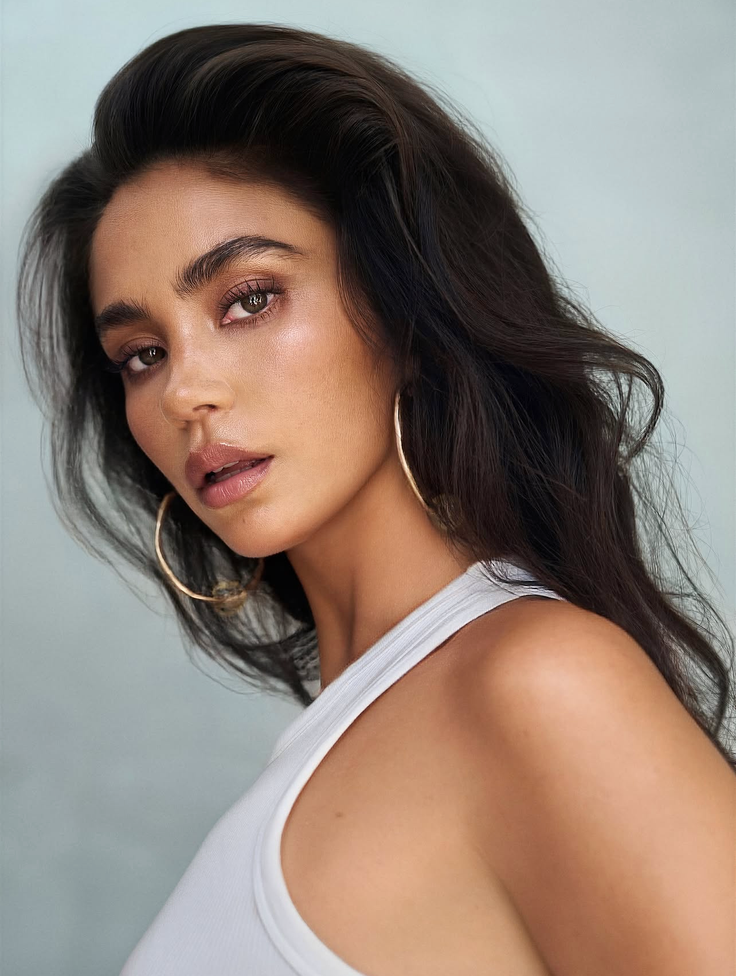 Woman with long dark hair and hoop earrings in a white tank top