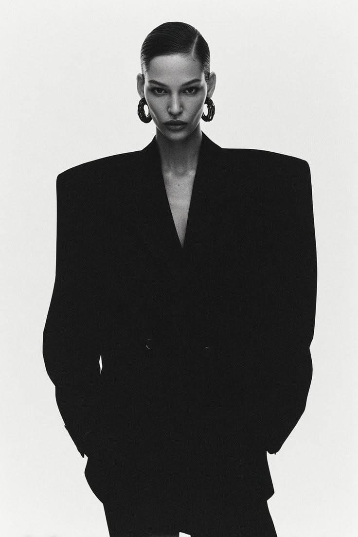 Woman in a black blazer with slicked back hair and large earrings