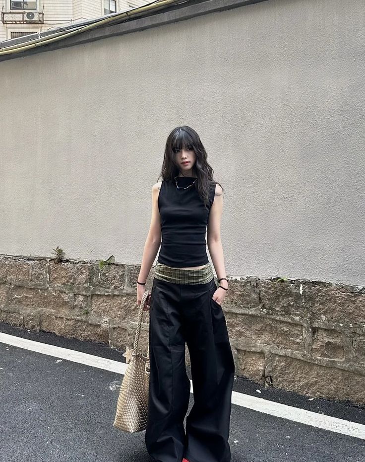 Woman with long black hair wearing a black top and wide leg pants on a street