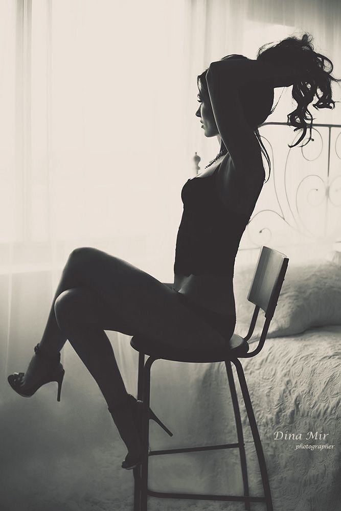 Woman in silhouette sitting on a chair in a bedroom, wearing high heels