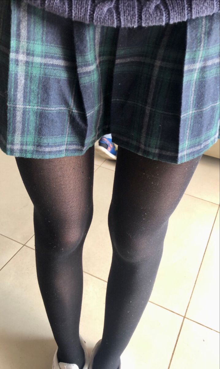 Lower body of a person wearing a plaid skirt, black tights, and white sneakers