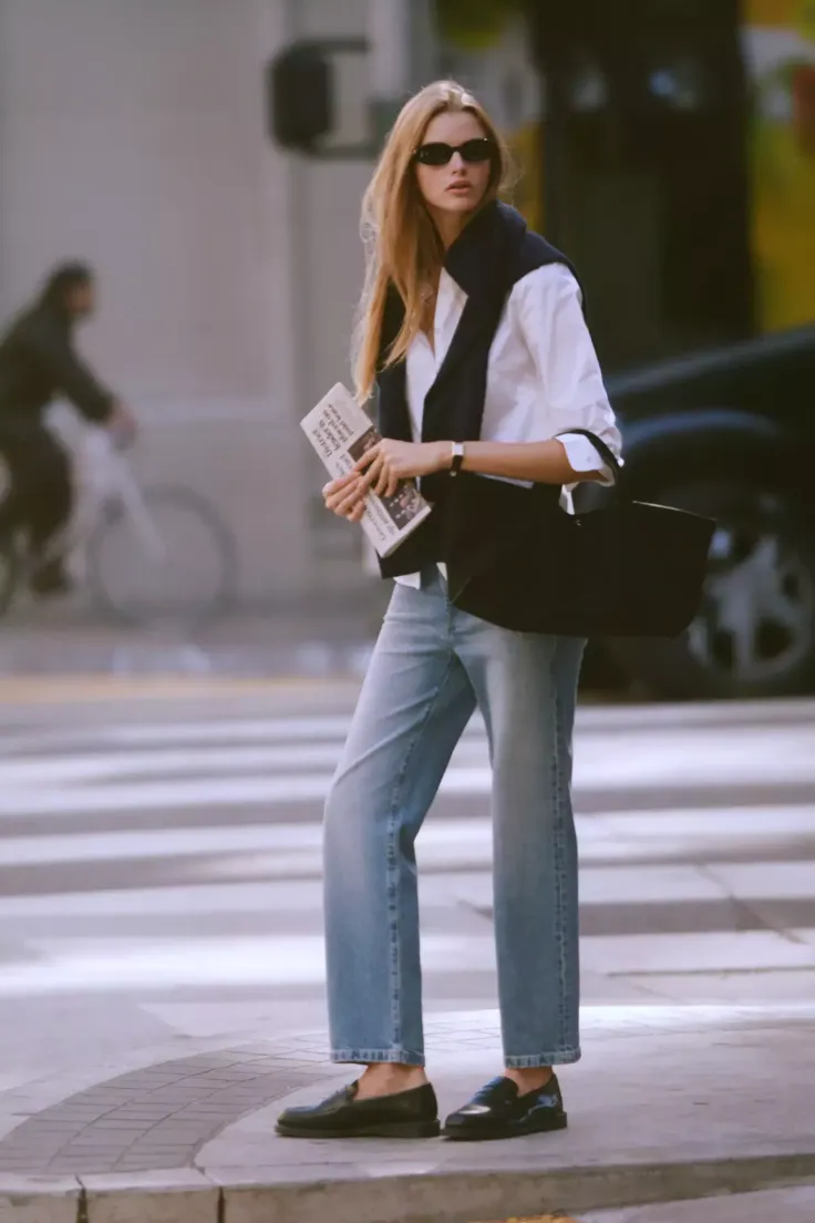 Woman in sunglasses, white shirt, and jeans standing on a city street