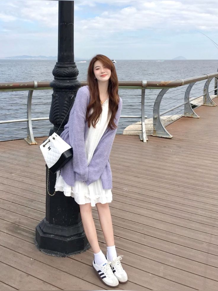 Woman in a white dress and purple cardigan standing on a pier by the ocean