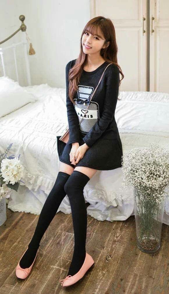 Woman with long hair in a black dress and thigh-high socks sitting on a bed
