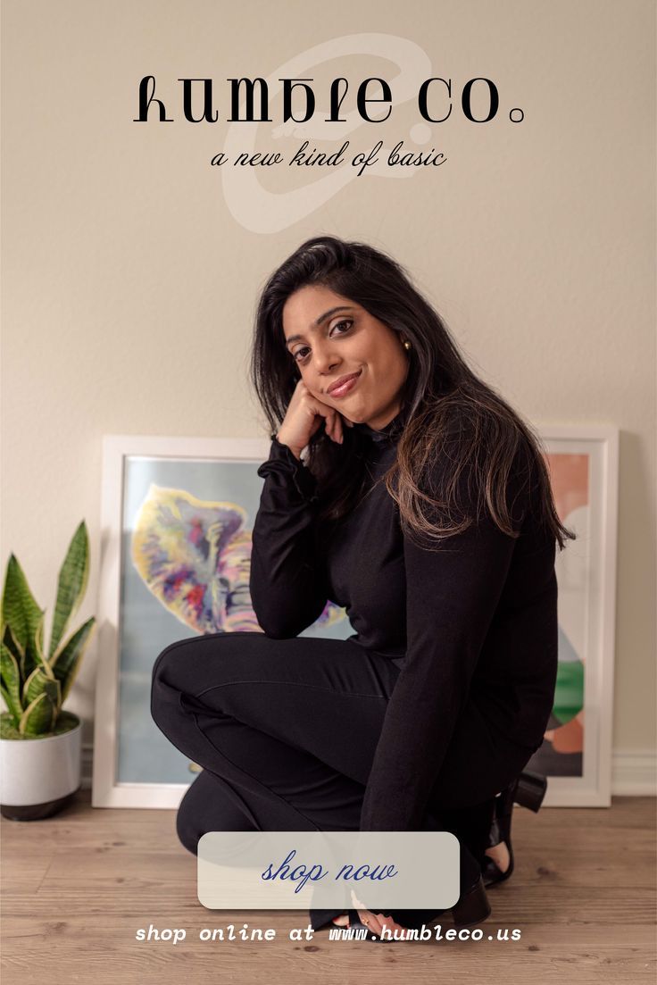 Woman in black top and pants crouching indoors with a plant and framed art