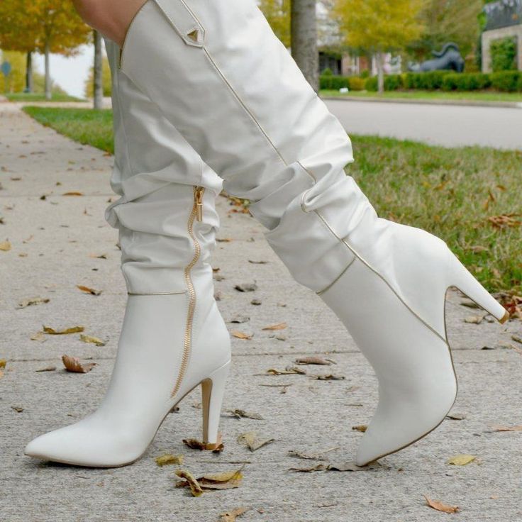 Person wearing white high-heeled boots with gold zippers on a sidewalk