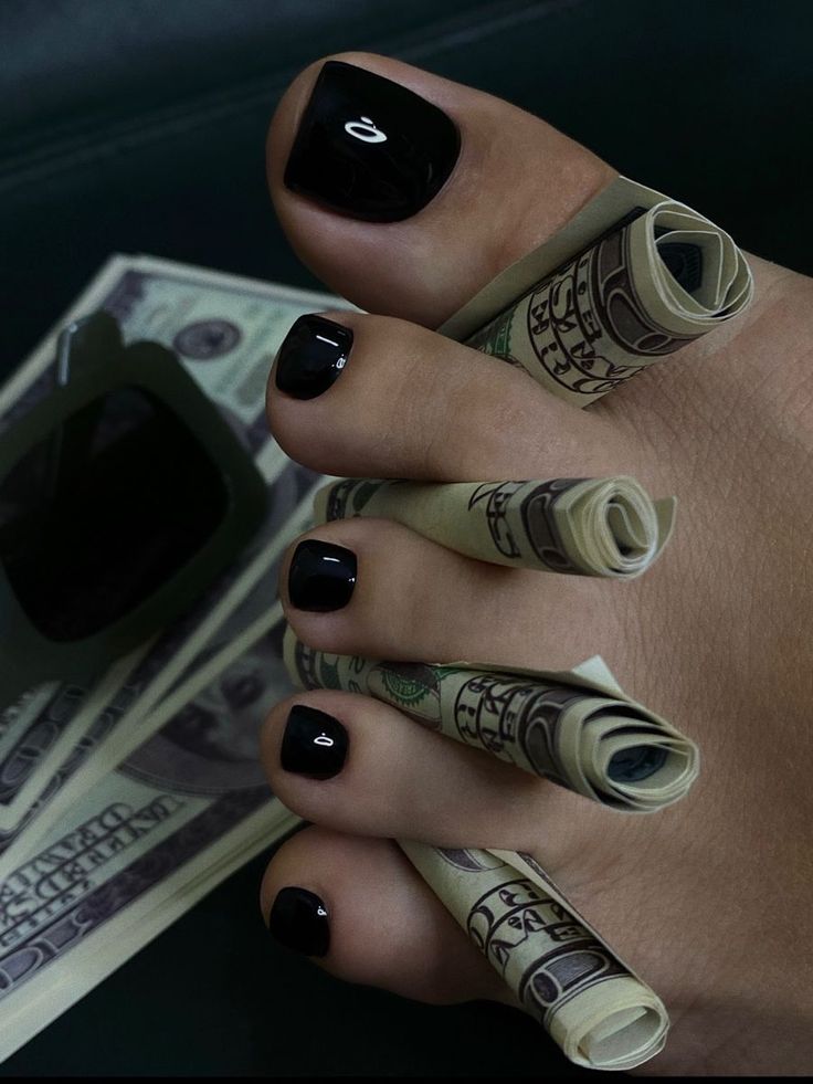 Foot with black pedicure and rolled money between the toes