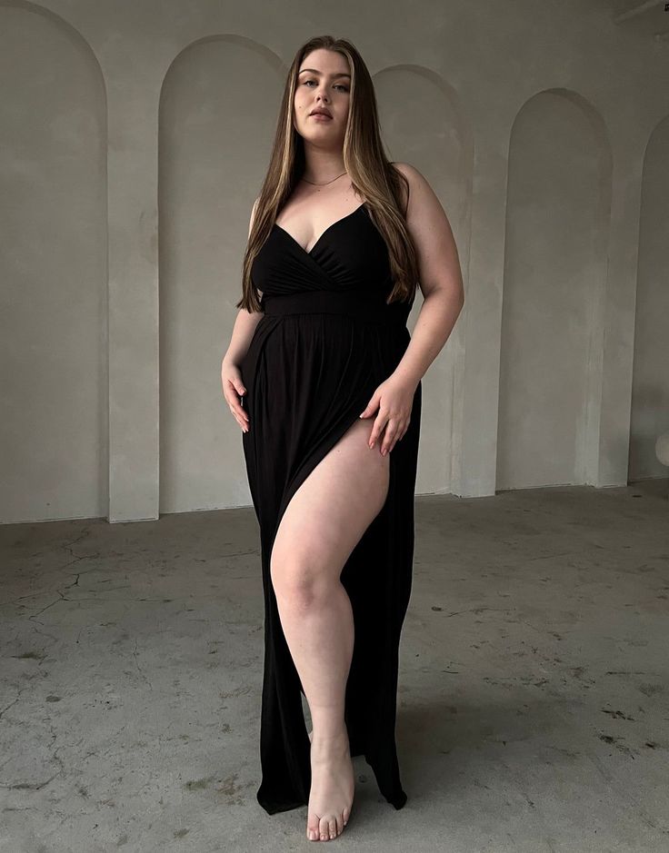 Woman in a black dress with a high slit and exposed cleavage indoors