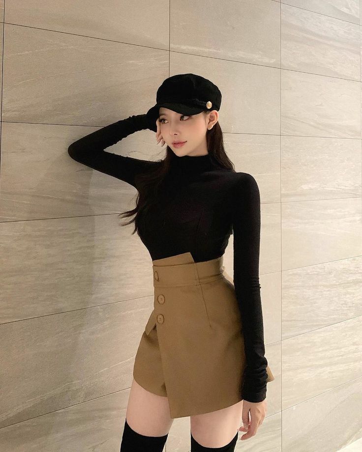 Woman in a black turtleneck and brown skirt with a newsboy cap indoors
