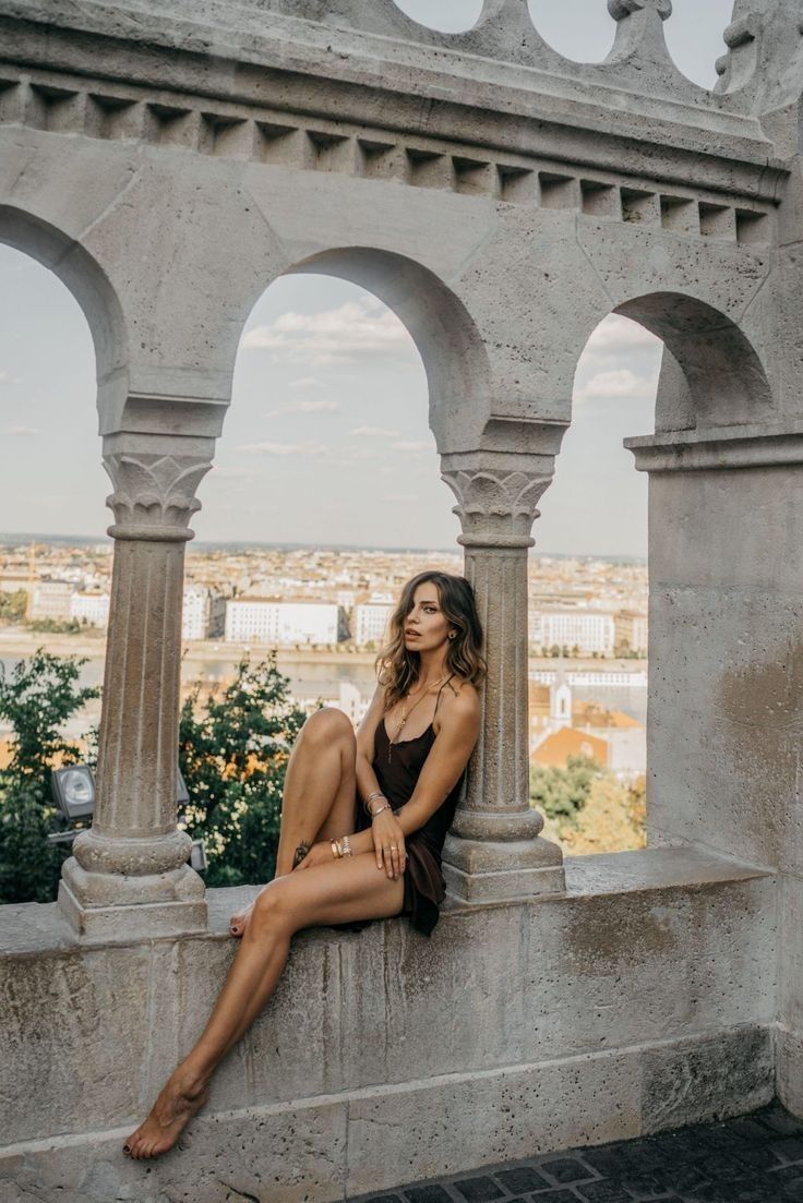 Woman in a dark dress sitting on a stone wall overlooking a city