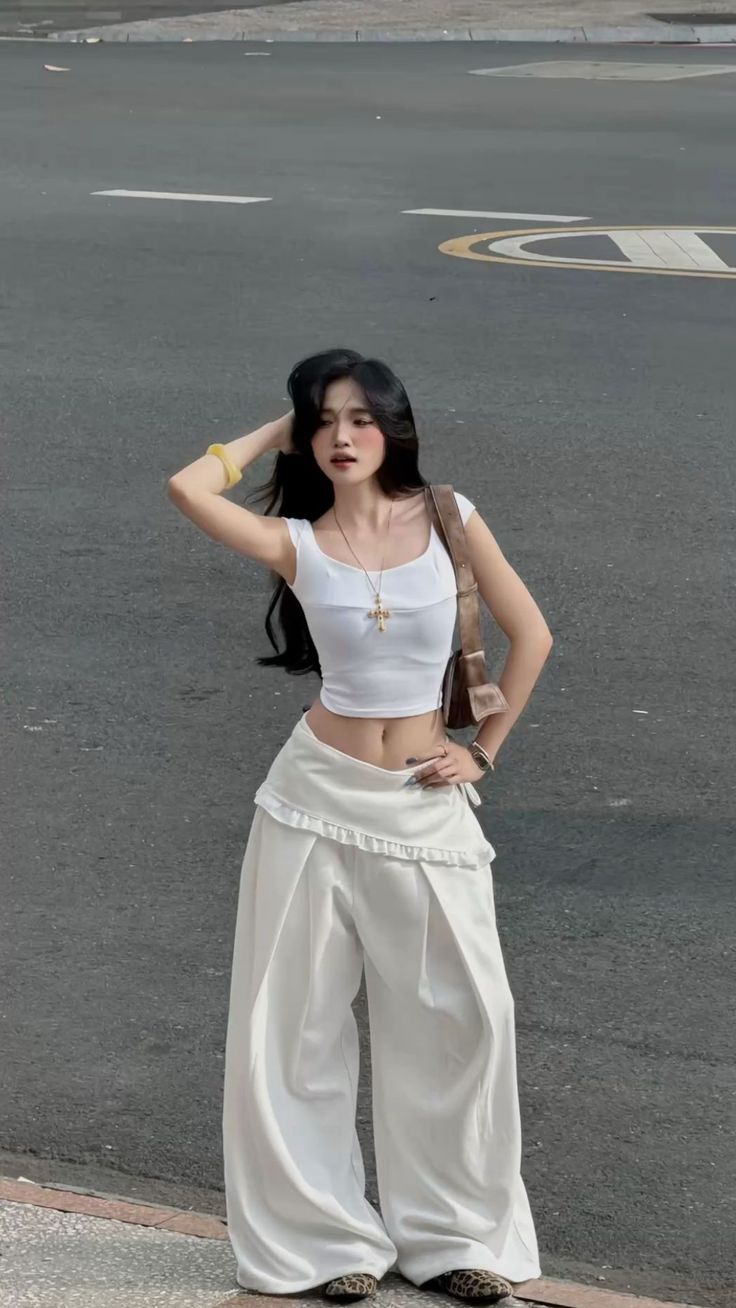 Woman with long black hair in a white crop top and wide leg pants on a street