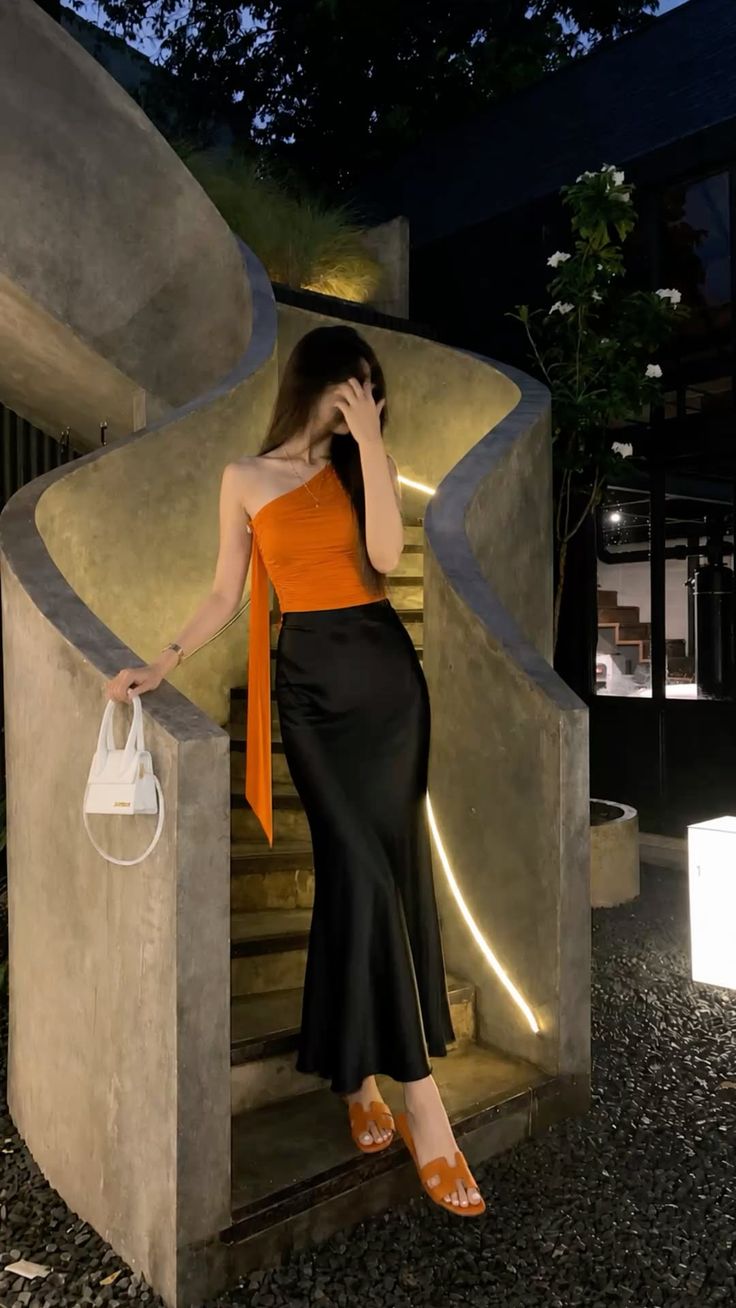 Woman in an orange top and black maxi skirt on a spiral staircase at night