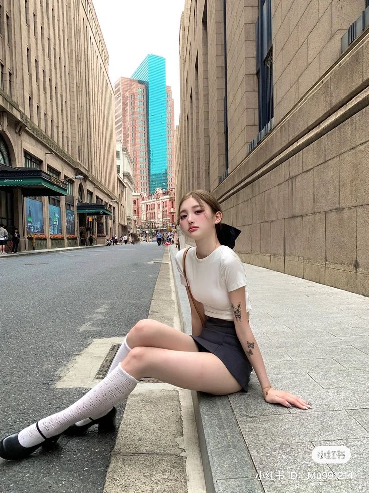 Woman in a short skirt and white socks sitting on a city sidewalk