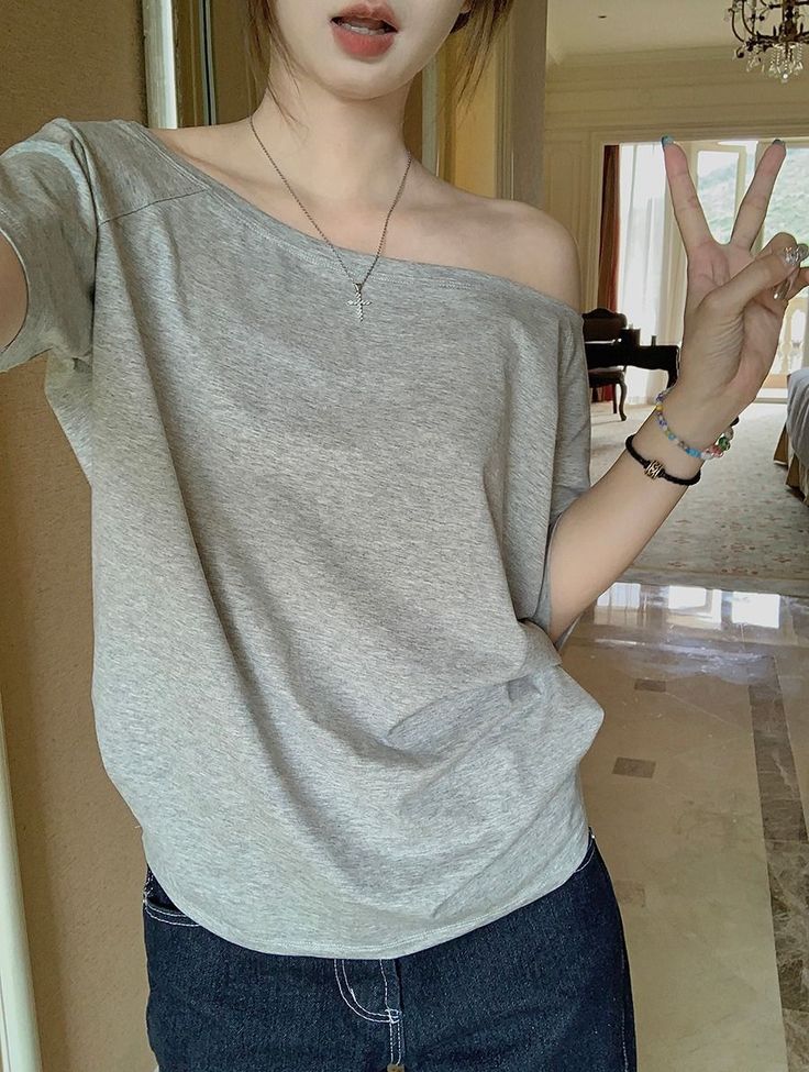 Person in an off-shoulder gray top and jeans making a peace sign