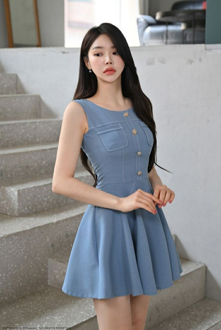 Woman in a light blue sleeveless dress standing indoors