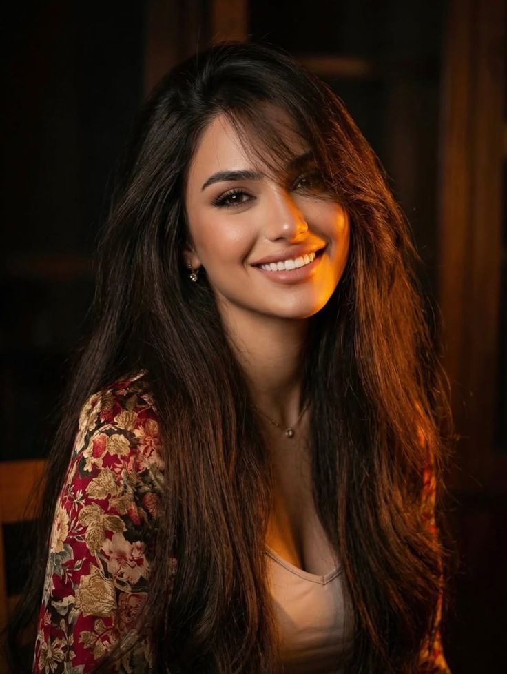 Woman with long dark hair and a floral top smiling with warm lighting