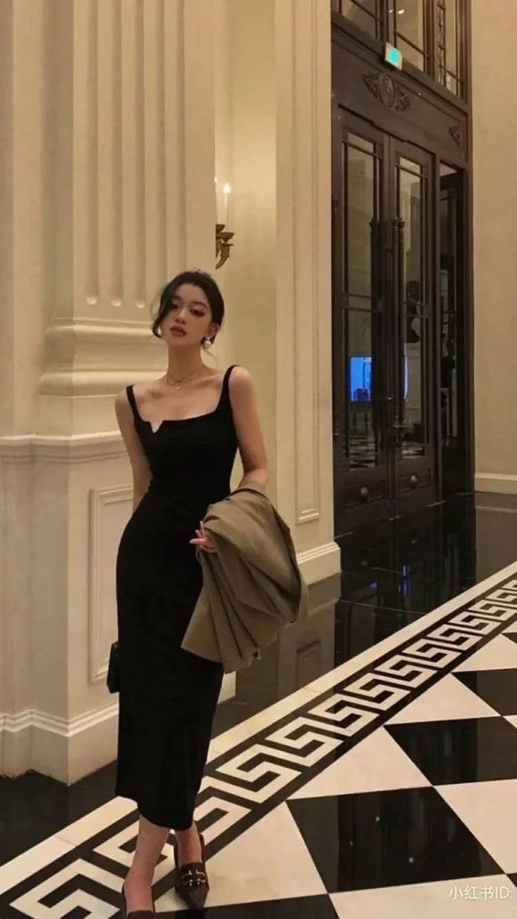 Woman in a black dress and high heels standing in an elegant indoor setting