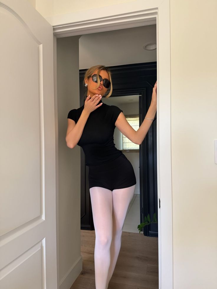 Woman in black top and white tights posing in a doorway