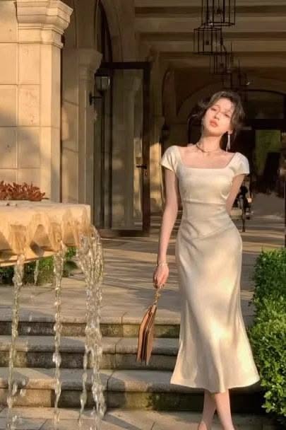Woman in a satin dress standing next to a fountain in soft golden hour light