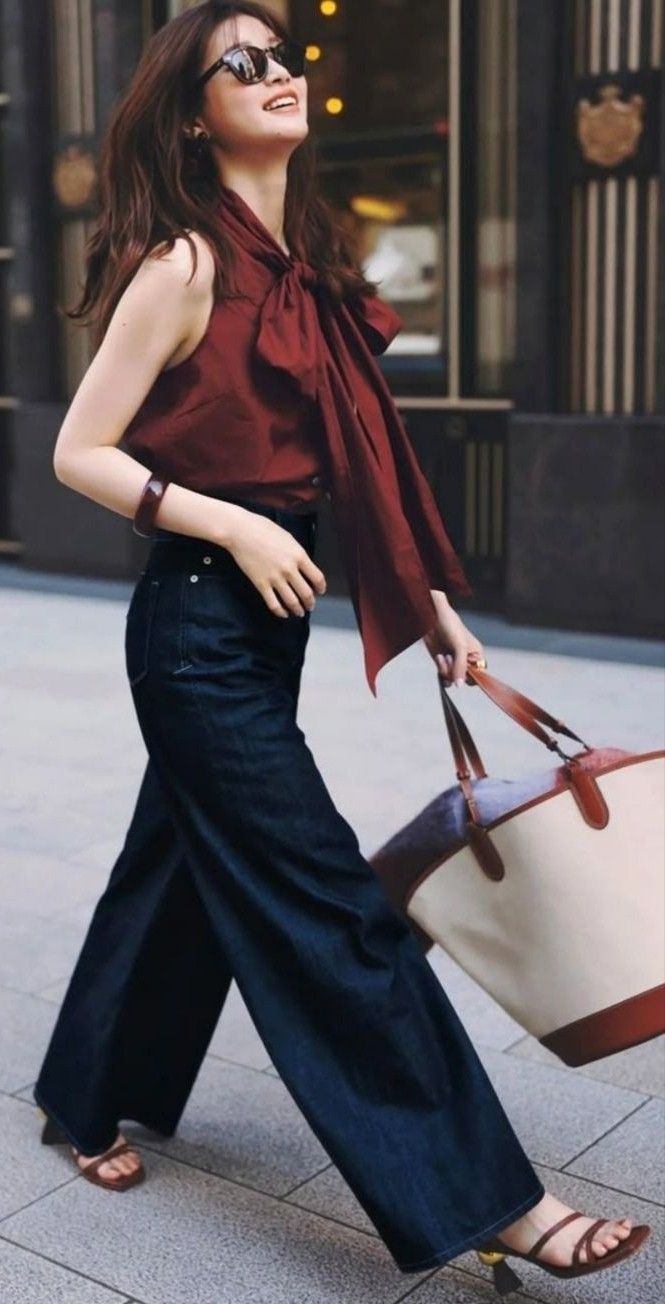 Woman in sunglasses, a sleeveless top, and wide leg jeans walking outdoors