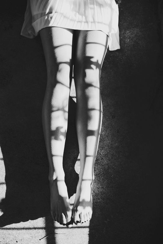 Bare legs in a white dress with grid shadows from a window in black and white